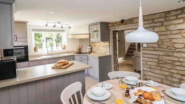 Una cocina moderna con una isla central, comedor con zona de desayuno y una pared de piedra.