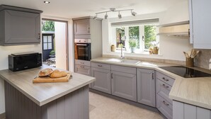 Una cocina moderna con armarios grises, horno empotrado, microondas y una isla grande con tabla de cortar y pan.