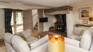 Una sala de estar con chimenea de piedra, un conjunto de sofás, un televisor montado en la pared y una escalera que lleva a un espacio exterior.