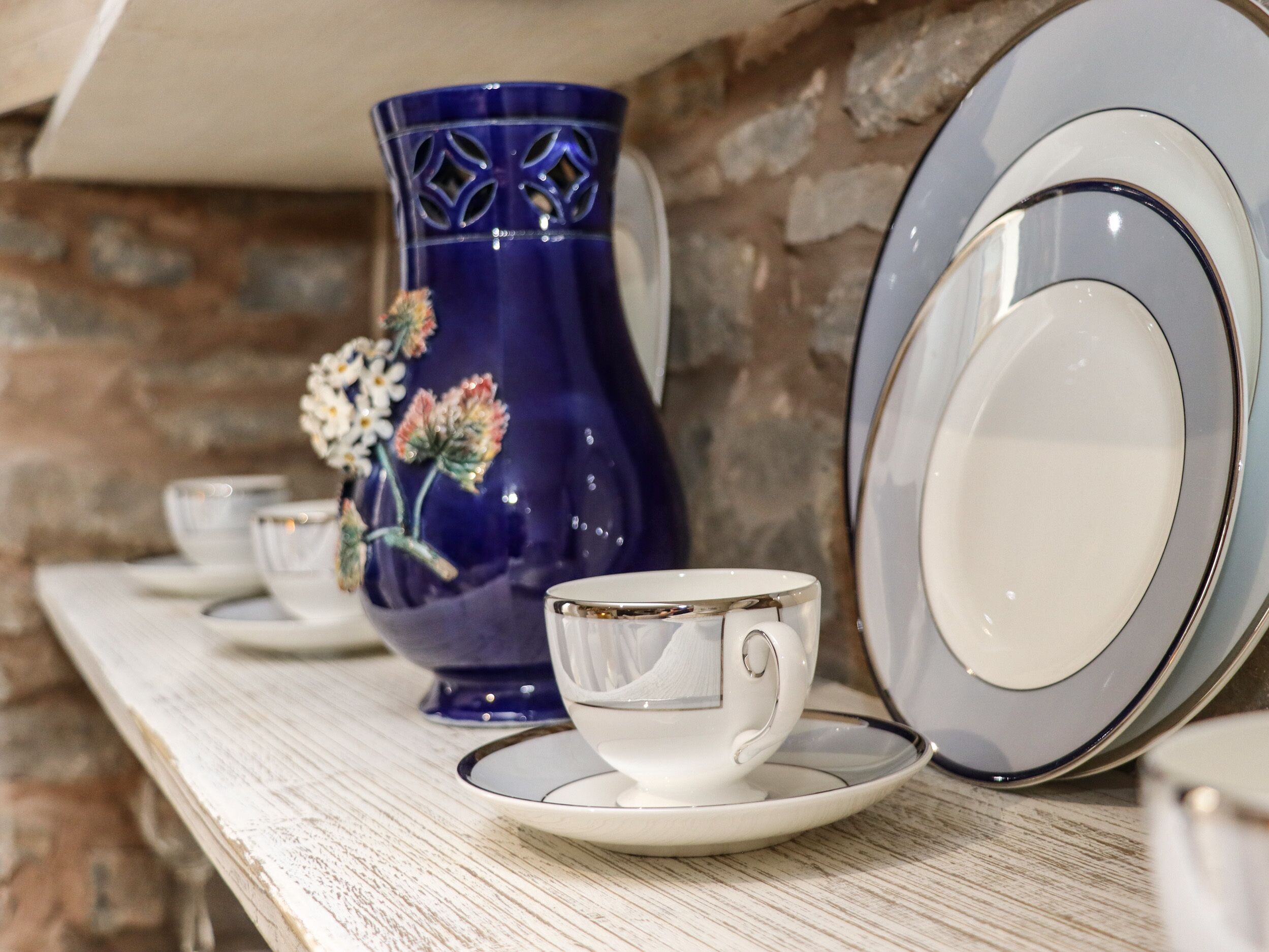 Un tavolo con una tazza e un piattino bianchi, un vaso blu con motivi floreali e piatti impilati.