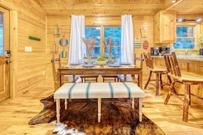 A wooden cabin interior with a dining table set for four, a bench, and a fur rug on the floor.