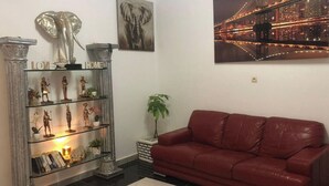 A living room with a red leather sofa, a glass display cabinet with figurines, and a cityscape painting.