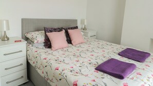 Ein ordentlich bezogenes Bett mit Blumenmuster, zwei Nachttische mit Lampen und eine weiße Kommode mit Schubladen.