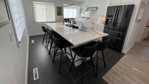 Una cucina moderna con isola centrale, sgabelli neri, frigorifero in acciaio inossidabile e mobili bianchi.