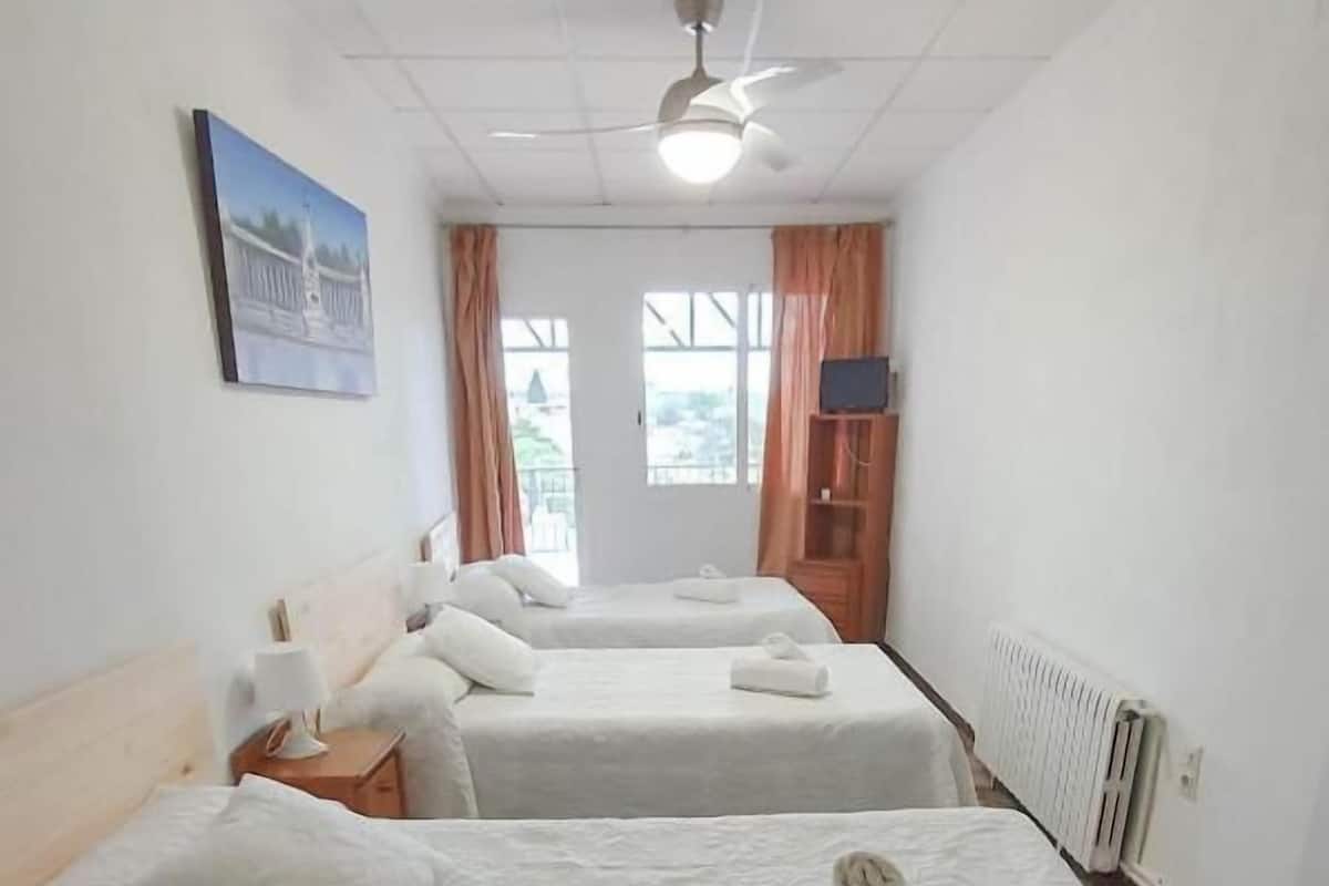 Une chambre d’hôtel avec deux lits, un ventilateur de plafond, un radiateur et une fenêtre avec des rideaux.