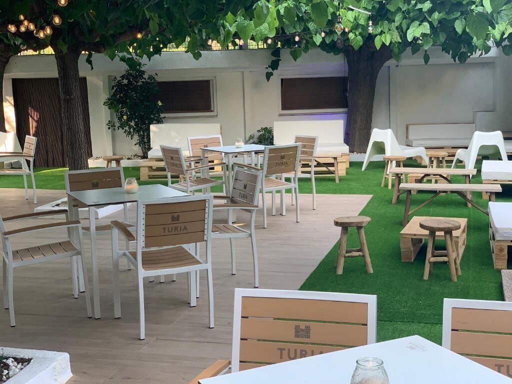 An outdoor seating area with tables and chairs, surrounded by greenery and trees.