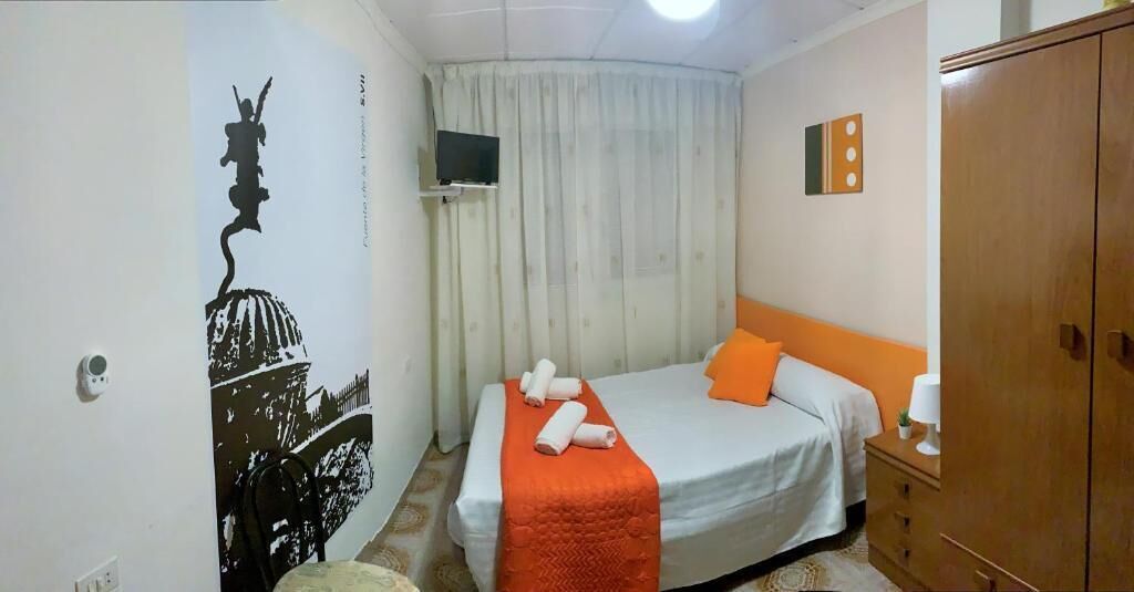 Un dormitorio con cama, armario, televisor y cortina.