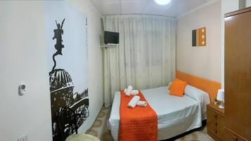 Un dormitorio con cama, armario, televisor y cortina.