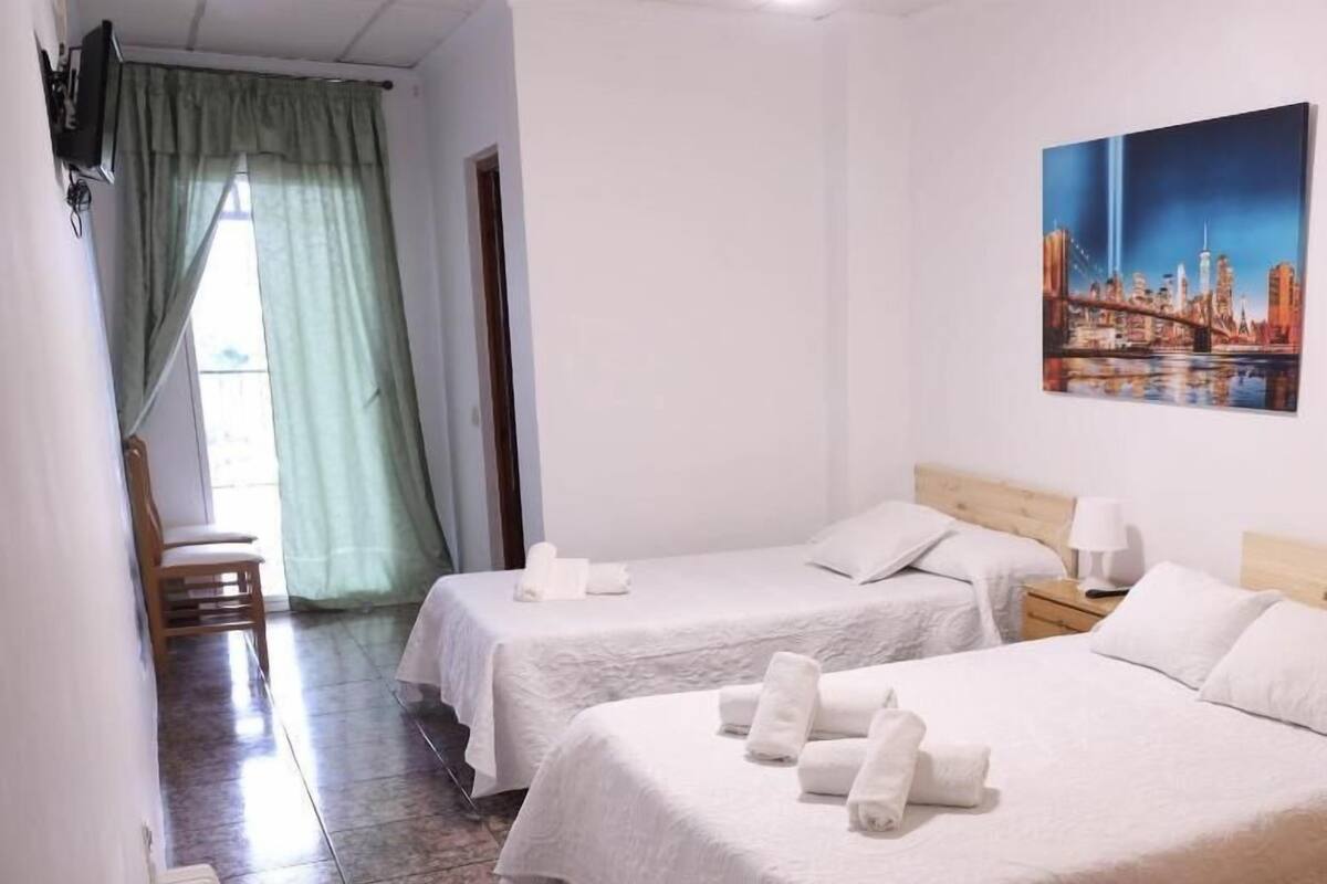 Une chambre d’hôtel avec deux lits, un tableau au mur et une chaise près de la fenêtre.