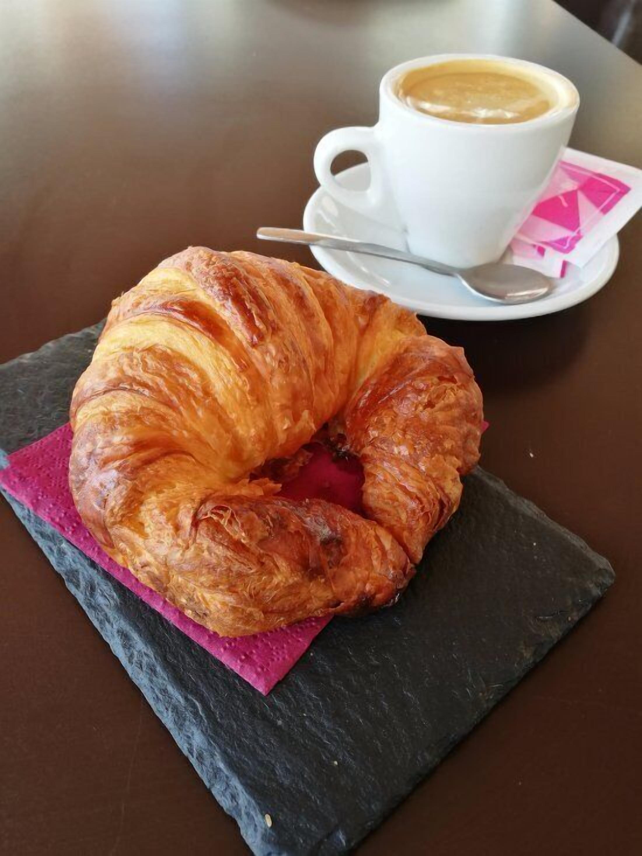 A croissant on a slate board with a cup of coffee on a saucer.