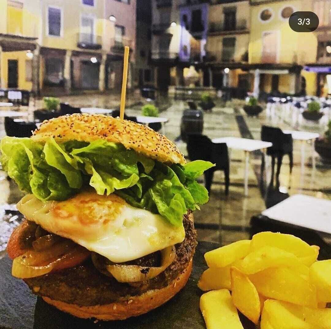 Un hamburger con lattuga, formaggio e un panino ai semi di sesamo, servito con patatine fritte.