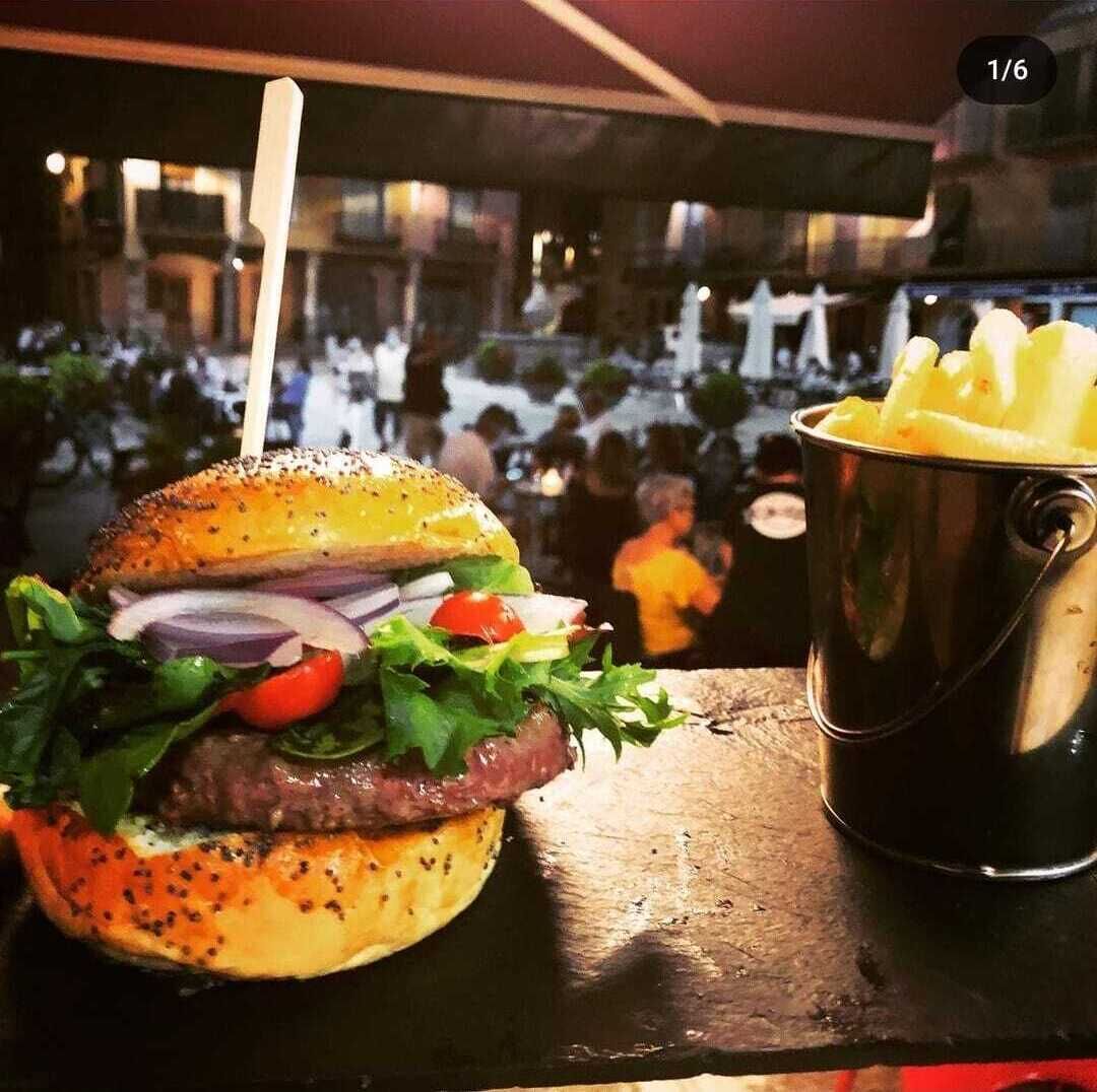 A burger with a bun, lettuce, tomato, onion, and a meat patty, accompanied by a bucket of fries.