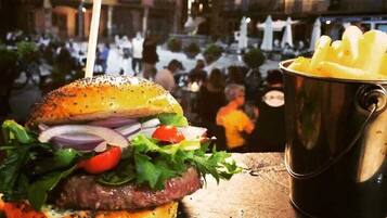 A burger with a bun, lettuce, tomato, onion, and a meat patty, accompanied by a bucket of fries.