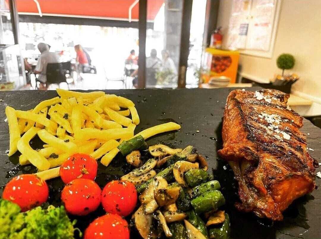 Plato negro con carne a la parrilla, papas fritas y verduras.