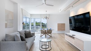 A modern living room with a grey sofa, a round coffee table, a dining area with chairs, a TV, and a balcony with a view. - Homity Exclusive Ab-3-c6-2d (Motril)