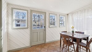 Ein Zimmer mit Holzvertäfelung, einem großen Fenster, einem Esstisch mit Stühlen und einer Tür.