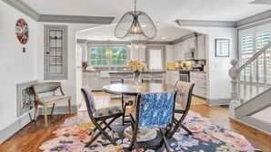 A dining area with a round table, chairs, and a floral rug. There is a kitchen in the background with cabinets and a microwave.