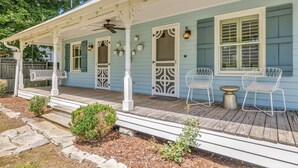 A porch with a wooden deck, white railings, and two white chairs.