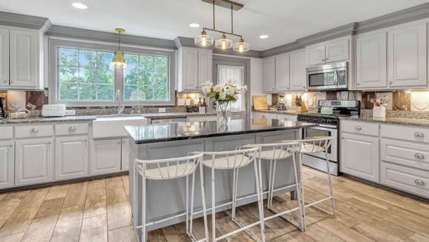 A spacious kitchen with white cabinetry, a large island with bar stools, a stainless steel oven, and a microwave.