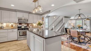 A spacious kitchen with white cabinetry, a large island, stainless steel appliances, and a wooden floor.