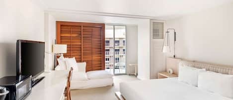 Une chambre d’hôtel équipée d’un lit, d’une télévision, d’un bureau avec un ordinateur, d’une chaise et offrant une vue sur la ville grâce à une grande fenêtre.