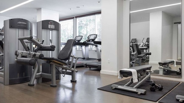 Un gimnasio moderno con máquinas de cardio, estaciones de pesas y un espejo grande.