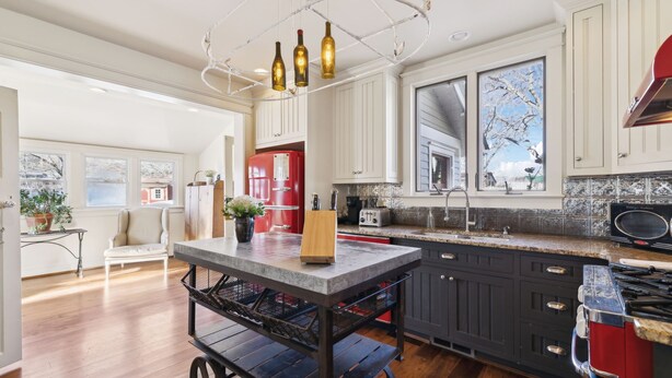 Una cocina con una isla central, muebles oscuros, un refrigerador rojo y un ventanal con vistas a árboles.