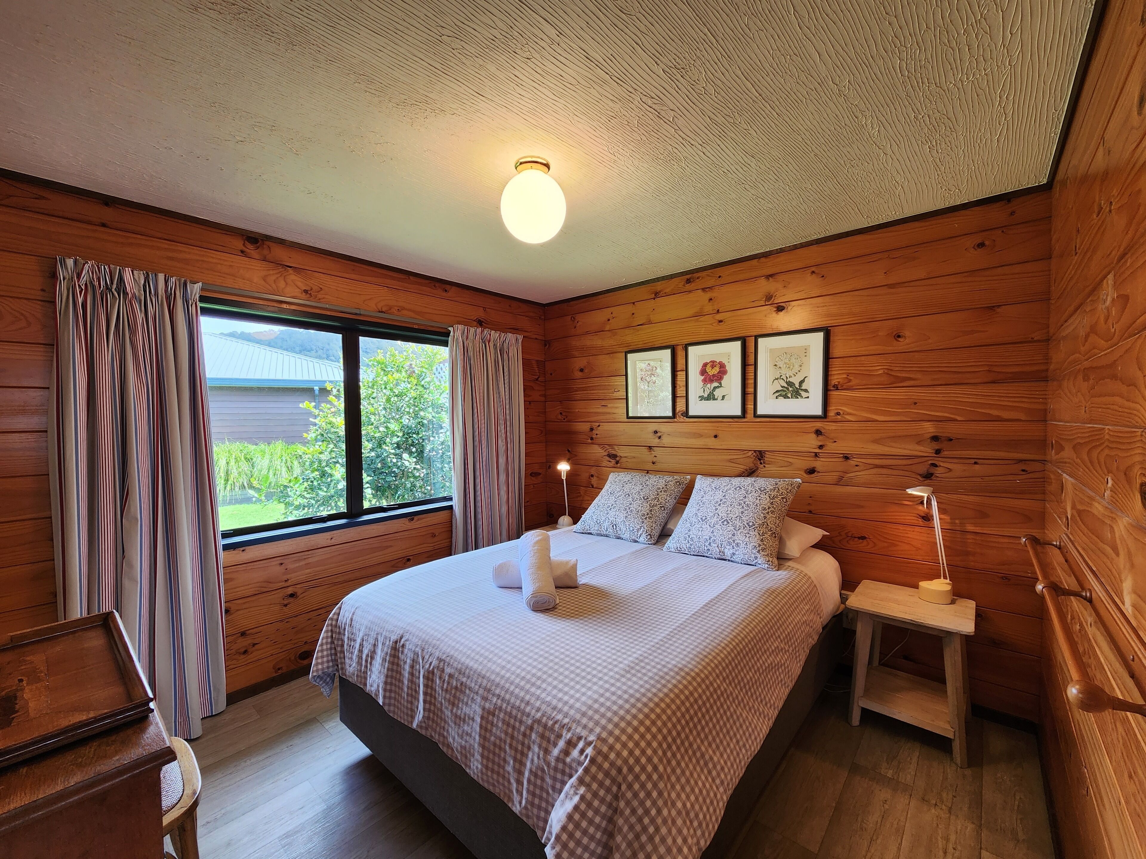 Quarto com painéis de madeira, cama, cortinas, mesa de cabeceira e obras de arte emolduradas na parede.