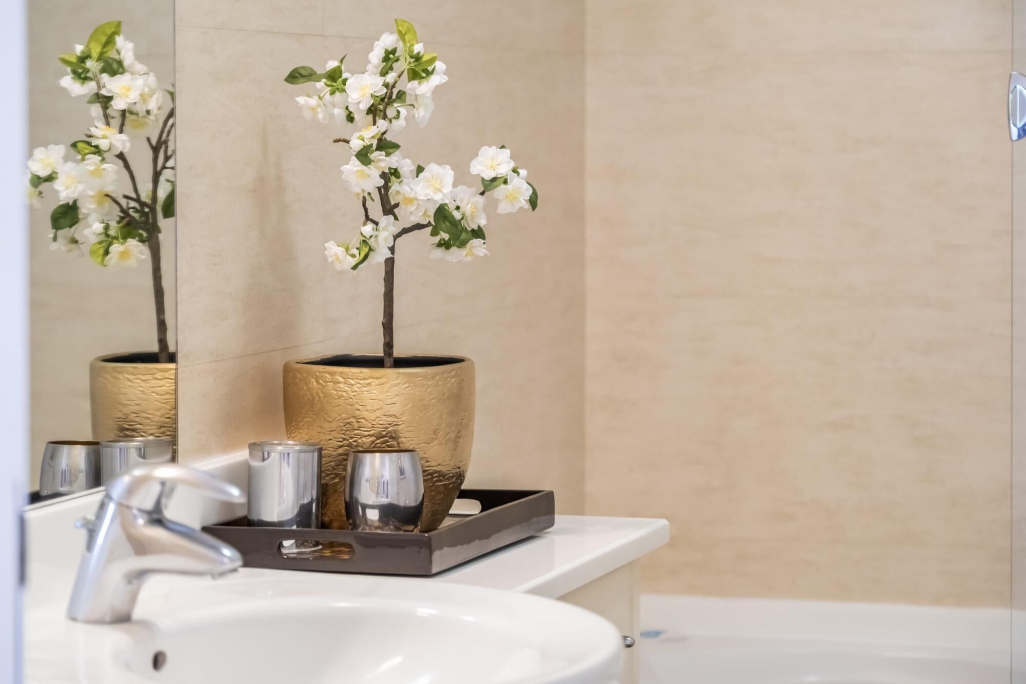 Un baño con un lavamanos blanco, un espejo y dos orquídeas blancas en macetas doradas.