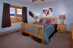 Une chambre à coucher avec un lit en bois, deux tables de chevet avec des lampes, une fenêtre avec des rideaux et une œuvre d’art accrochée au mur.