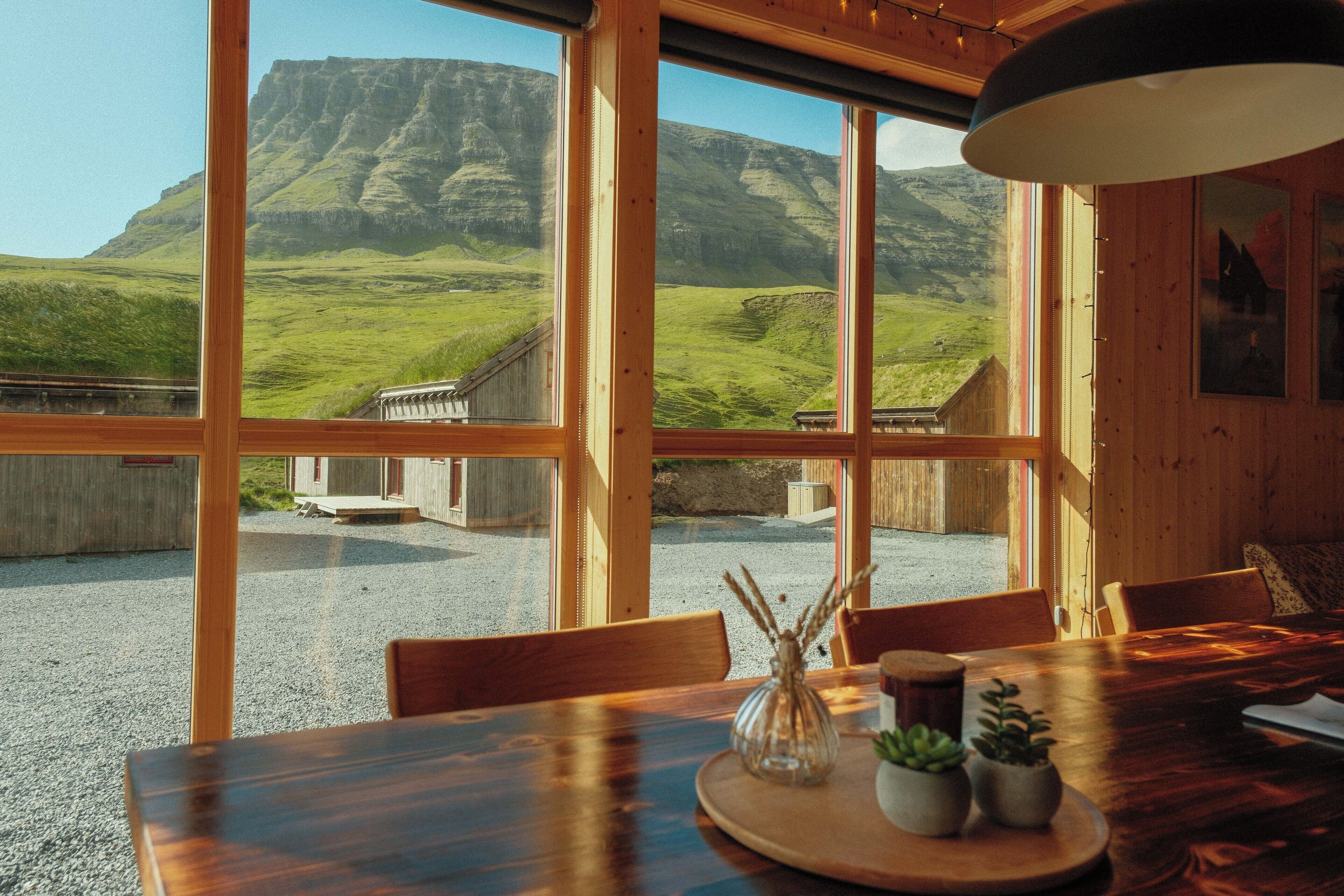A dining area with a wooden table, chairs, and a view of a mountainous landscape through large windows.