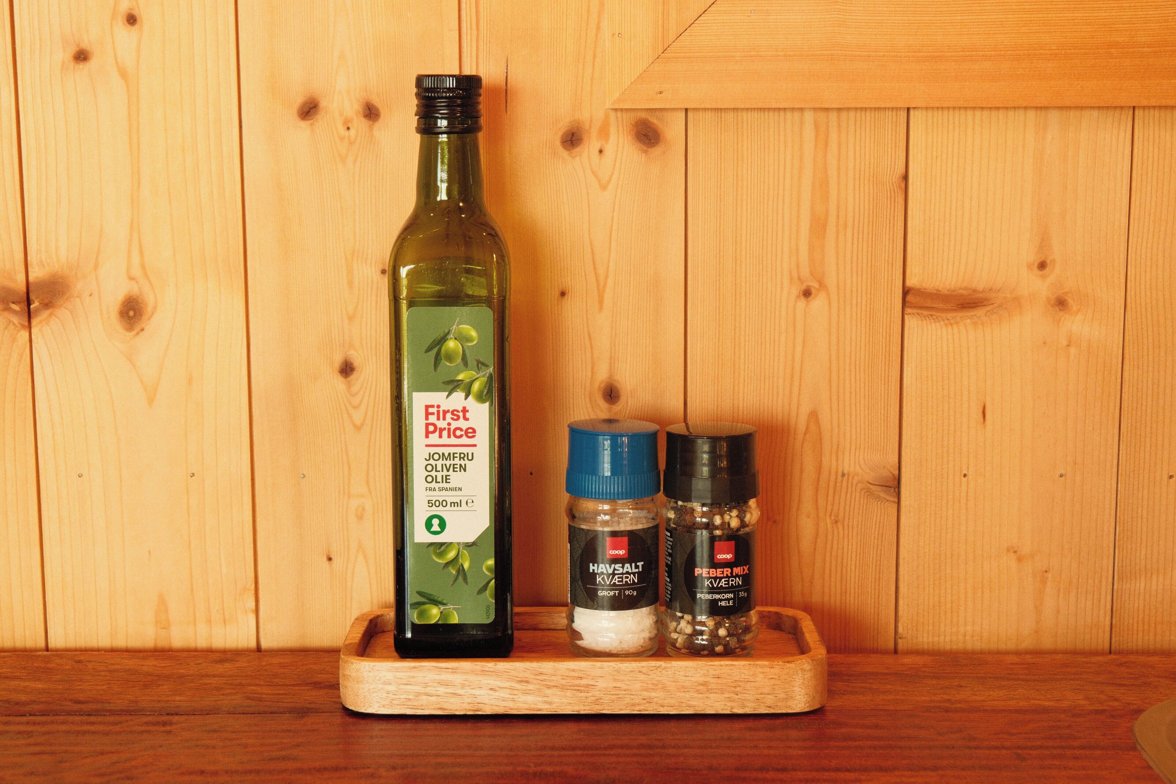 A wooden shelf with a bottle of olive oil, a salt shaker, and two pepper containers.