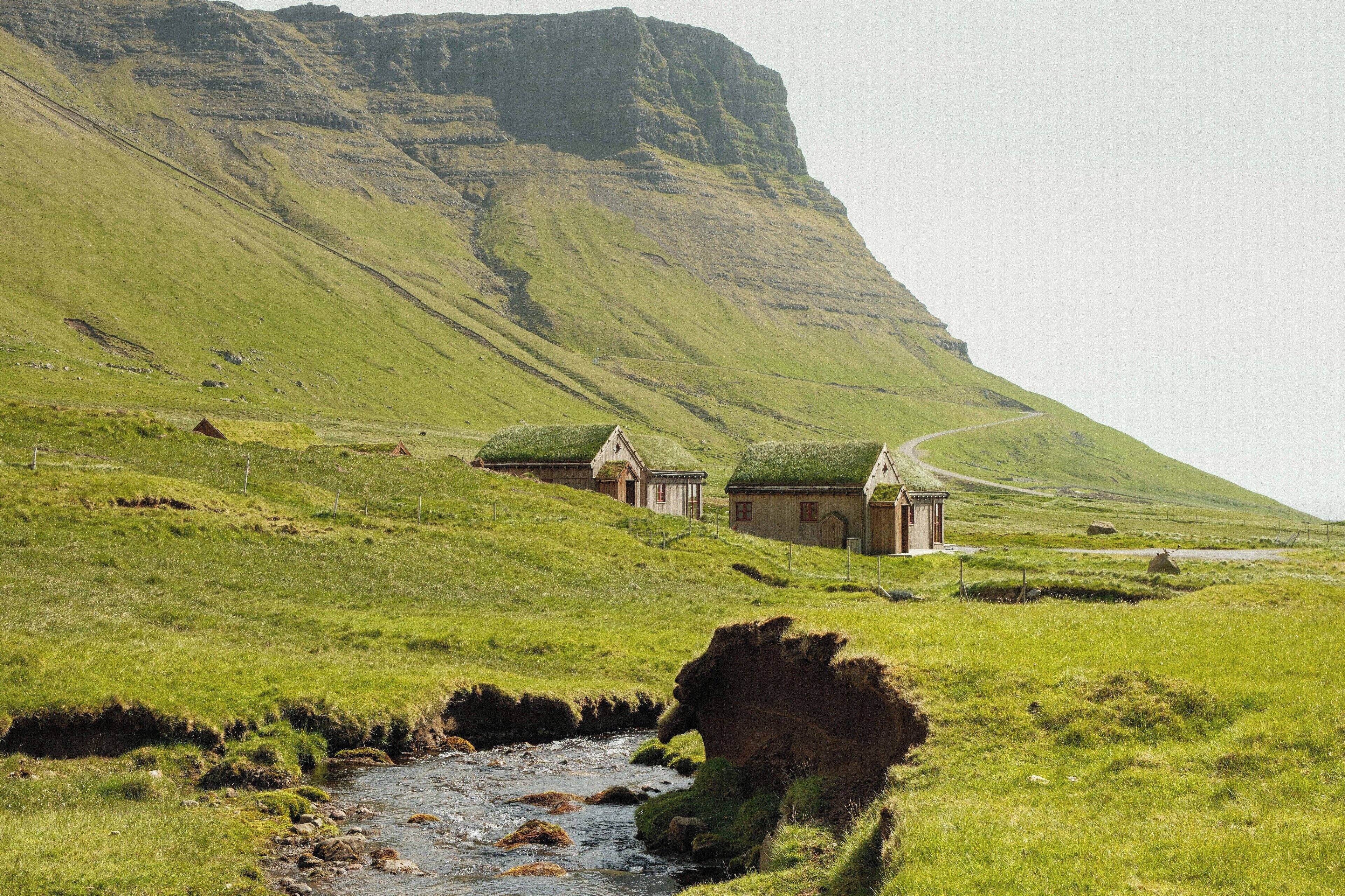 A rural landscape with a stream, grassy fields, and a few traditional houses with thatched roofs.