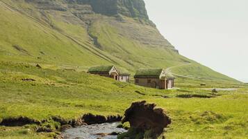 A rural landscape with a stream, grassy fields, and a few traditional houses with thatched roofs.