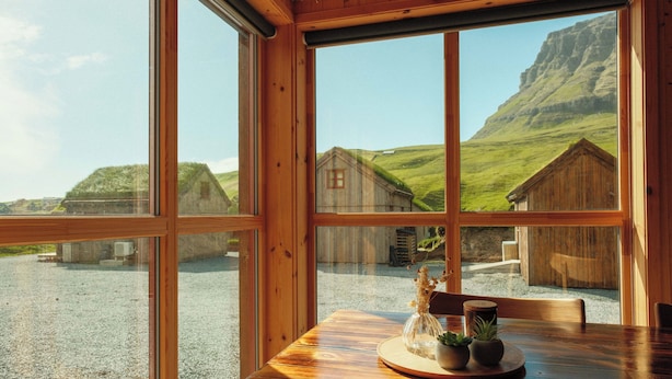 Interior de madera con amplios ventanales que dan a un paisaje rural con casas y una montaña.