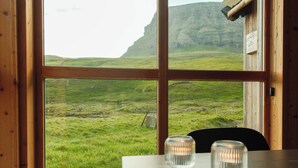 Habitación con un ventanal grande que ofrece vistas a un paisaje verde y acantilados. Hay una mesa de madera con dos candelabros de cristal transparente.