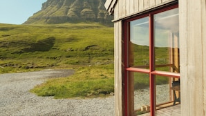 Un edificio de madera con ventanas amplias, un camino de grava y un paisaje con césped, con una formación rocosa destacada al fondo.