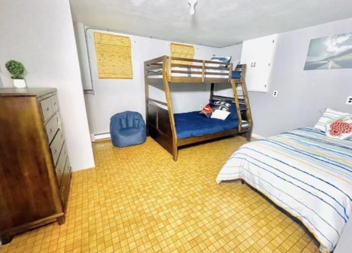 A bunk bed room with a wooden dresser and a blue chair.
