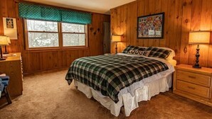 A cozy bedroom with a plaid bedspread, a window with a view of trees, and a wall-mounted painting.
