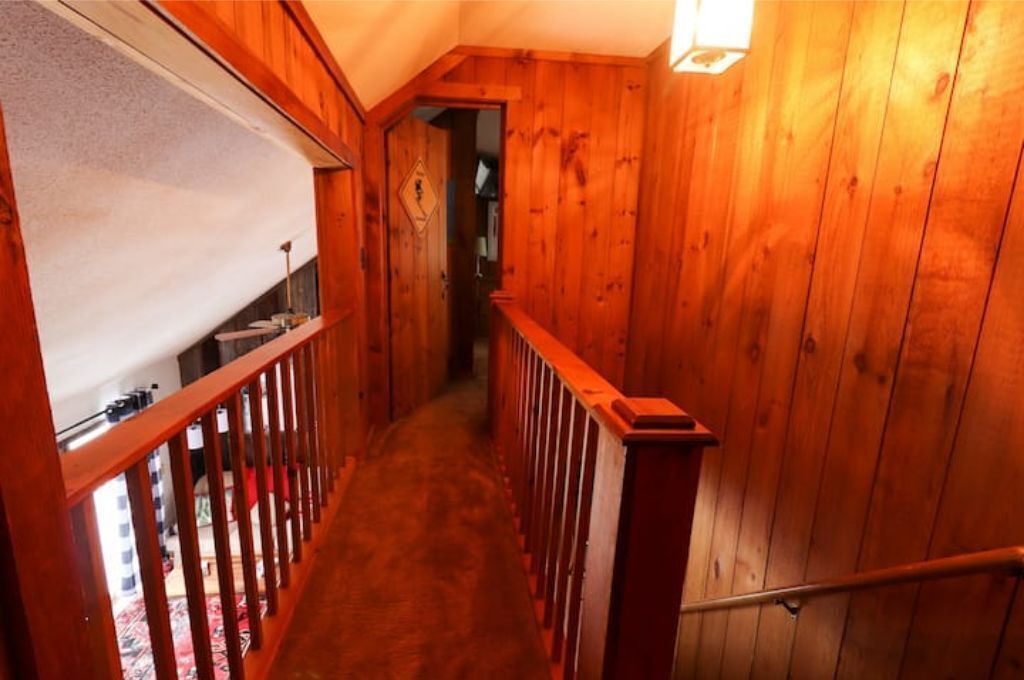 A wooden interior hallway with a carpeted floor and a wooden railing.