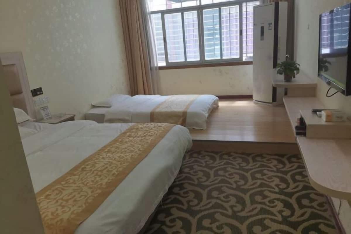 Une chambre d’hôtel avec deux lits, un bureau, une télévision et une fenêtre avec des stores.