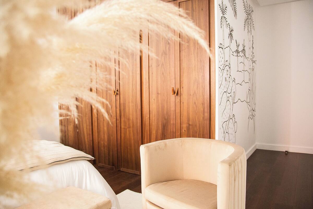 Un dormitorio con un armario de madera, una silla blanca y una pared con un mural floral.
