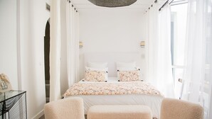 Une chambre à coucher avec un lit, deux tables de chevet et une fenêtre ornée de rideaux légers.