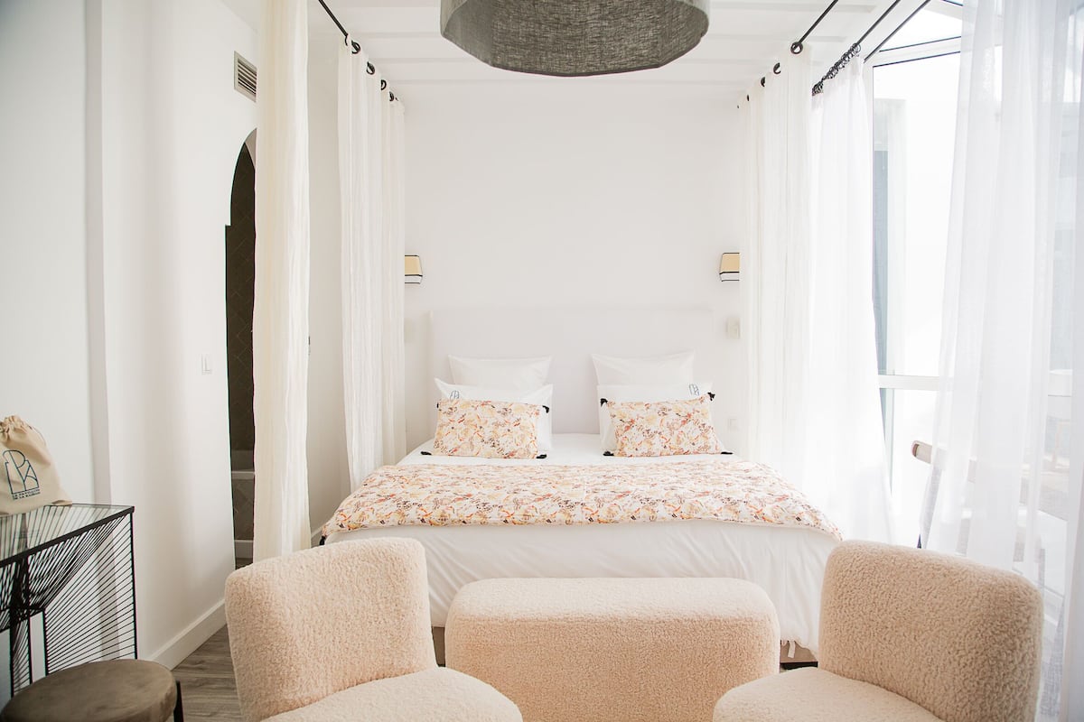 Un dormitorio con una cama, dos mesitas de noche y un ventanal con cortinas translúcidas.