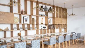 Un coin repas avec une table en verre et des chaises à motifs, des étagères en bois ornées d’objets décoratifs et des lampes suspendues.