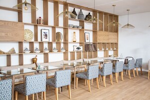 Un comedor con una mesa de vidrio y sillas estampadas, estantes de madera con adornos y lámparas colgantes.