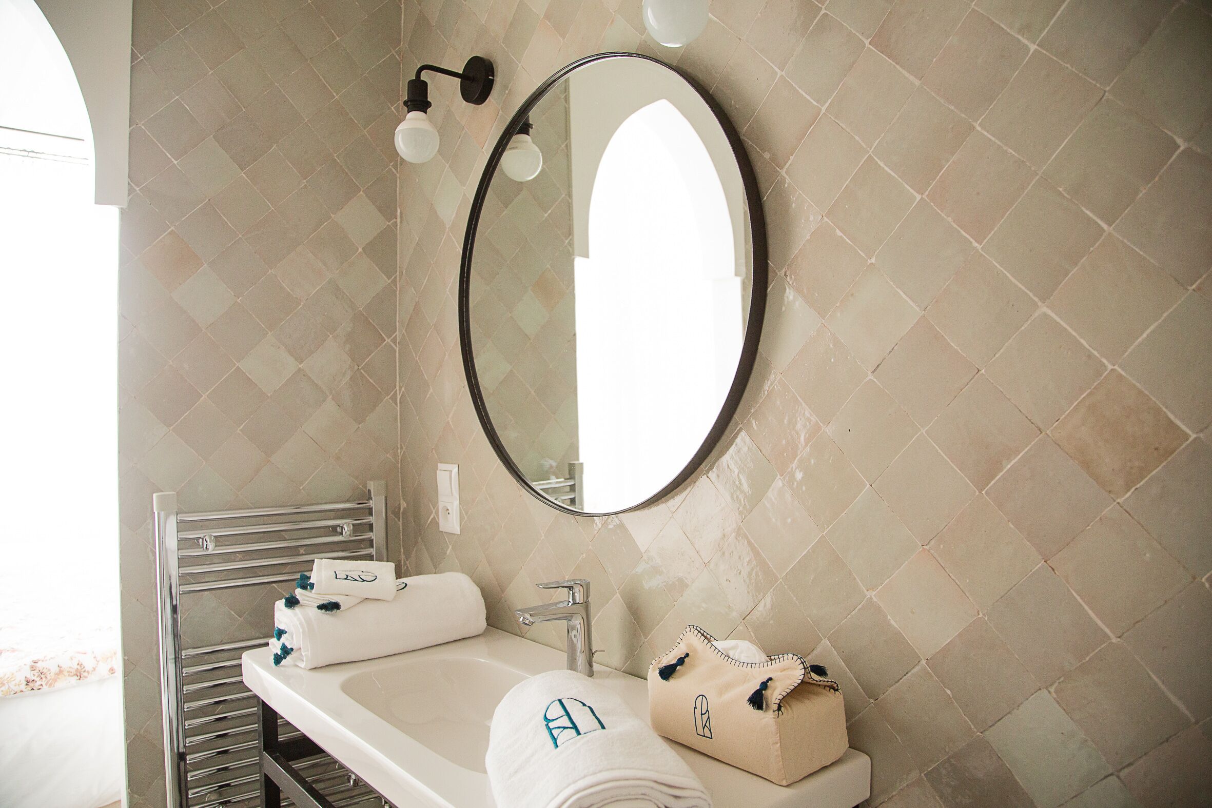 A bathroom with a round mirror, a sink, and a towel rack.