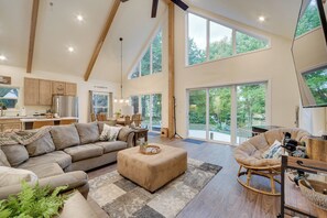 A spacious living room with a large sectional sofa, a rocking chair, and a dining area with natural light from large windows. - Waterfront Webster Cabin w/ Dock on Warner Lake! (Webster)