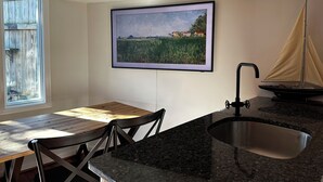 Ett kök med en bänkskiva i granit, en diskho i rostfritt stål, ett matbord med stolar och en inramad landskapsmålning på väggen.