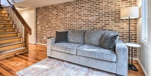 Ein Zimmer mit grauem Sofa, einer Holztreppe und einer Ziegelwand.